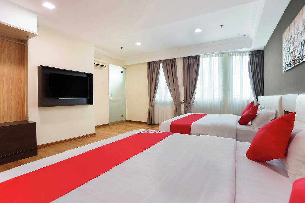 A hotel room with two beds, a flat-screen TV, and a large window with curtains.