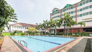 A swimming pool surrounded by palm trees and buildings with a red roof and green walls. - Collection O Hotel Super Cowboy (Malacca City)