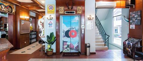 Um hall de hotel com um balcão de recepção, uma escadaria e um ar condicionado fixado na parede.