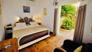 Ein Hotelzimmer mit Bett, Nachttischen, einem Sessel und Blick auf einen Garten durch eine Schiebetür.
