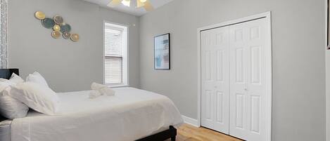 A bedroom with a bed, a ceiling fan, a window with blinds, and a white door.