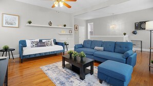 A modern living room with a blue sofa, a coffee table, and a ceiling fan. - Spacious 3-Bedroom with King Bed (St. Louis)