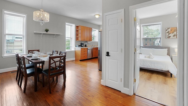 A spacious room with a wooden dining table, chairs, a chandelier, and a bed with white bedding. - Spacious 3-Bedroom with King Bed (St. Louis)