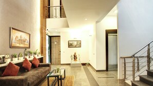 Un hall d’entrée moderne, avec un canapé, une table en verre, des plantes en pot et des œuvres d’art accrochées aux murs.