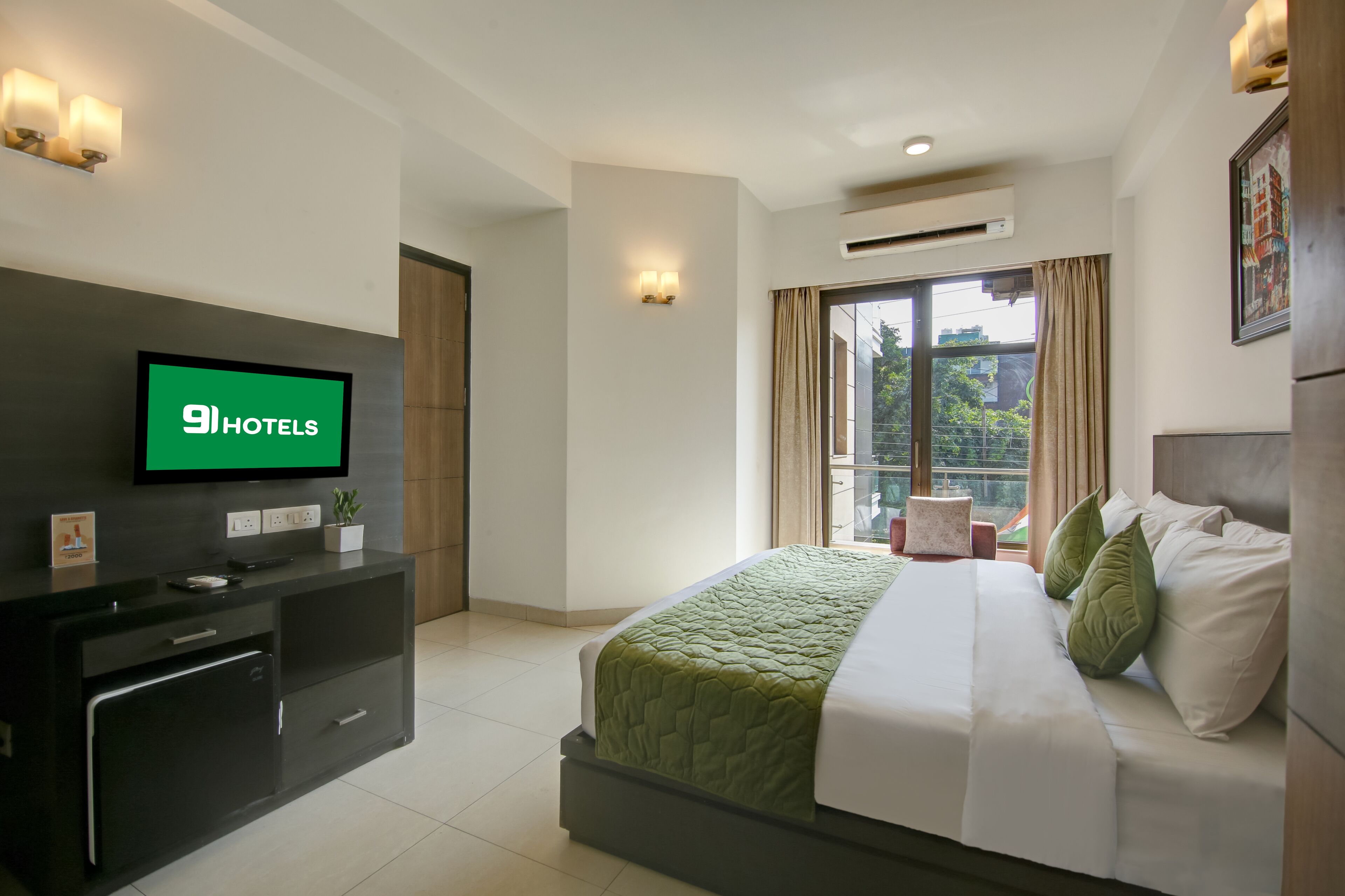 Une chambre d’hôtel avec un lit, un téléviseur fixé au mur, un bureau et une fenêtre avec des rideaux.