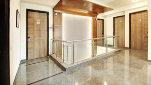 Un couloir d’hôtel moderne avec une rambarde en verre, des portes en bois et un plancher poli.