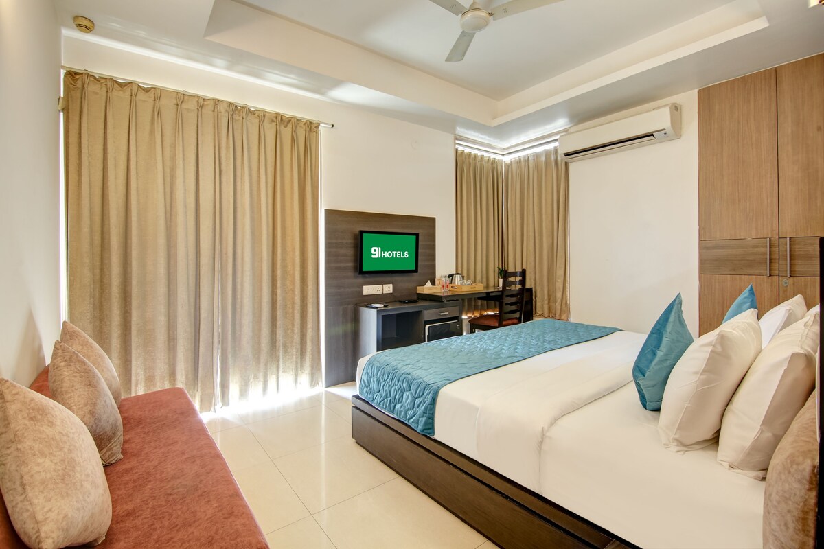 Quarto de hotel com cama, escrivaninha, televisão e cortinas.