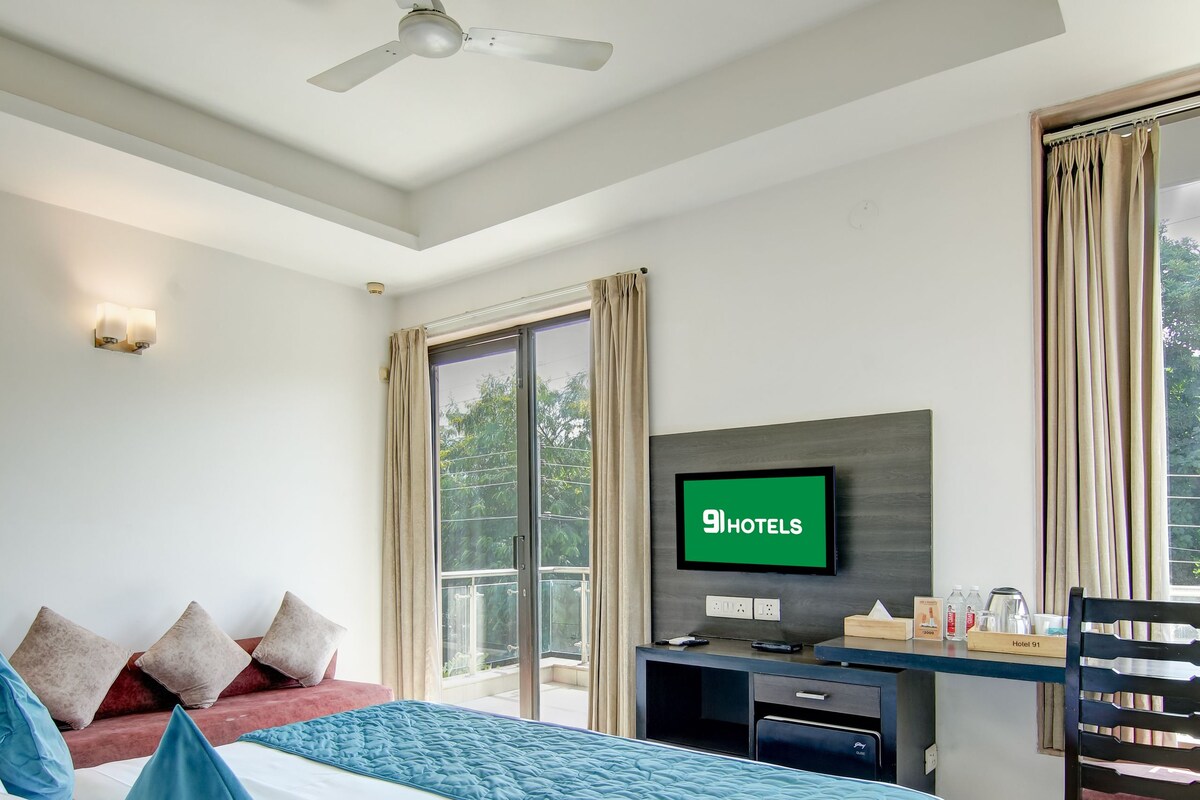 A hotel room with a bed, a desk, a television, and a balcony with curtains.