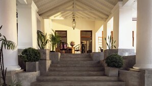 A grand staircase leading to a second floor, flanked by columns and potted plants, with a chandelier above.