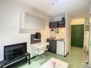 A compact living space with a kitchenette, a dining area with a white table and chairs, a flat-screen TV, and a green door. - Cozy studio in Lamalou, pets welcome, balcony and Wifi (Lamalou-les-Bains)