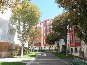 A building with a red and white facade, multiple balconies, and a central courtyard with a bench. - Cozy studio in Lamalou, pets welcome, balcony and Wifi (Lamalou-les-Bains)