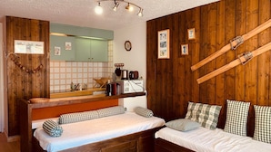 A compact room with two beds, a wooden wall, a mirror, and a kitchenette. - Spacious studio south balcony 4 pers, near slopes, parking (Pra-Loup)