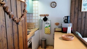 A kitchen with wooden cabinets, a sink, a stove, a trash can, and a coffee maker. - Spacious studio south balcony 4 pers, near slopes, parking (Pra-Loup)