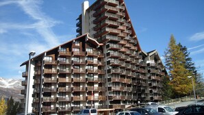 A multi-story hotel with numerous balconies, a prominent corner design, and a mountainous backdrop. - Spacious studio south balcony 4 pers, near slopes, parking (Pra-Loup)