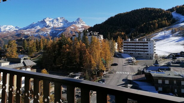 A mountain town with a view of snow-capped peaks, autumn trees, and a parking area with buildings in the foreground. - Spacious studio south balcony 4 pers, near slopes, parking (Pra-Loup)