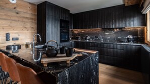 A modern kitchen with dark cabinetry, a marble countertop, and wooden accents.