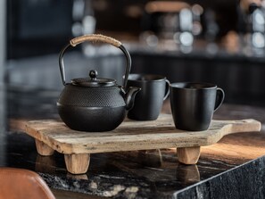 A black teapot with a textured handle on a wooden tray, accompanied by two black cups on a marble surface.