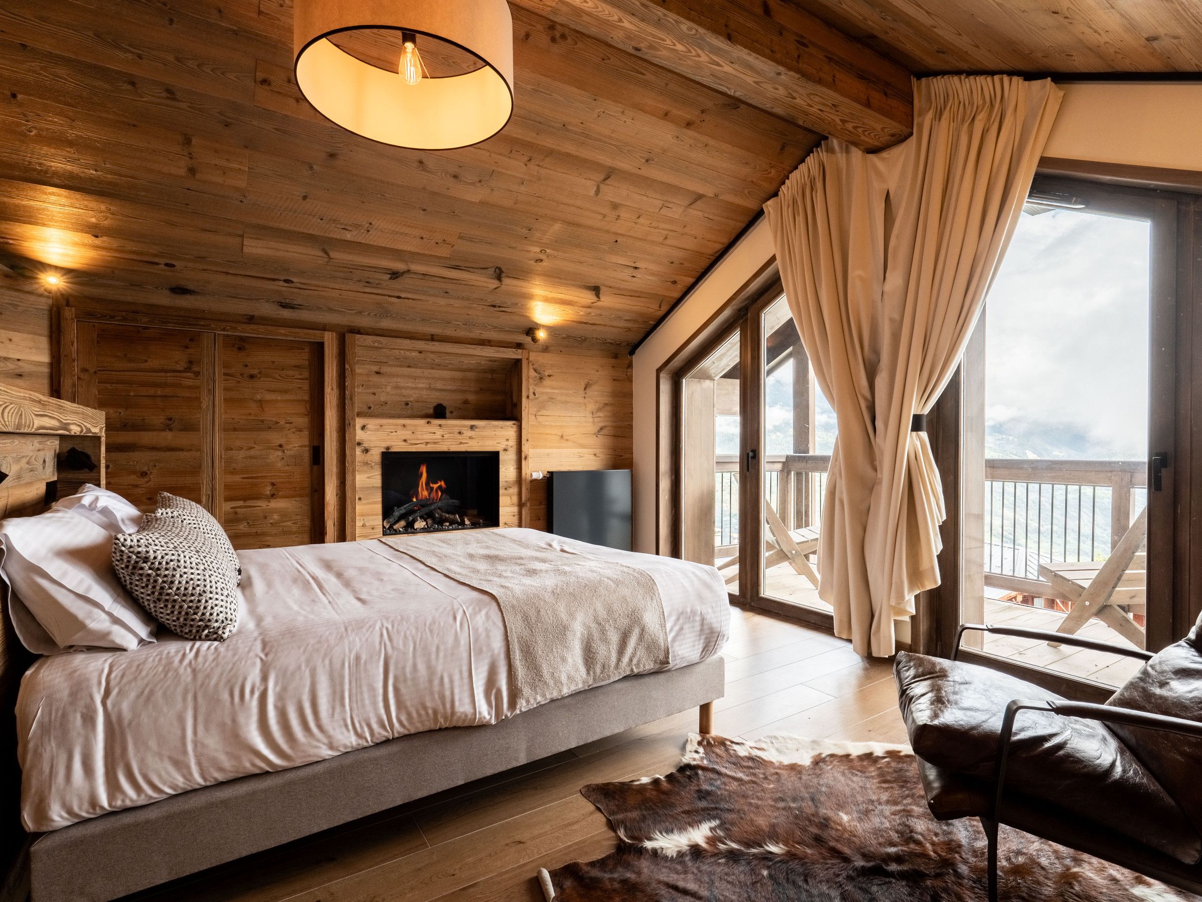 A cozy cabin-style bedroom with a bed, a fireplace, and a large window with curtains.