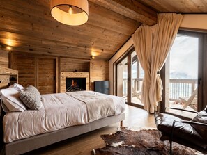 A cozy cabin-style bedroom with a bed, a fireplace, and a large window with curtains.