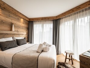 A bedroom with a wooden headboard, a bed with white linens, grey curtains, and a wooden nightstand with a lamp. - Luxury Apartment 170m², 5 Bedrooms, Ski Nearby, Parking, Wifi (La Plagne Montalbert)