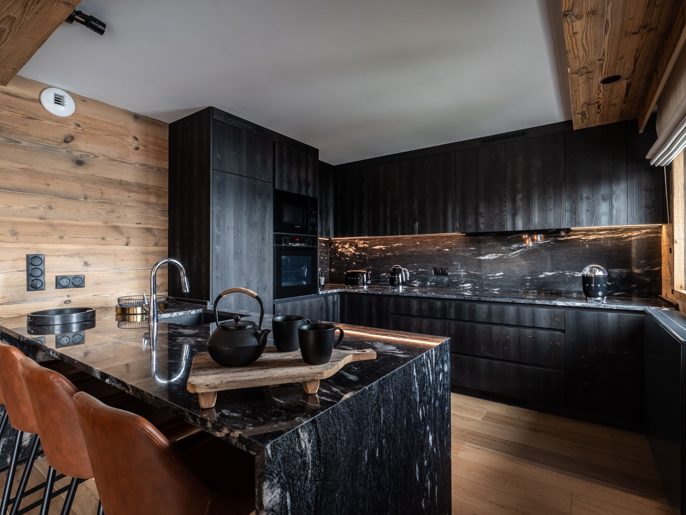 A modern kitchen with dark cabinetry, a marble countertop, and wooden accents. - Luxury Apartment 170m², 5 Bedrooms, Ski Nearby, Parking, Wifi (La Plagne Montalbert)