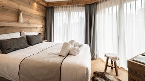 A bedroom with a wooden headboard, a bed with white linens, grey curtains, and a wooden nightstand with a lamp.