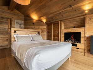 A wooden-paneled bedroom with a bed, a fireplace, and a wall-mounted TV. - Luxury Apartment 170m², 5 Bedrooms, Ski Nearby, Parking, Wifi (La Plagne Montalbert)