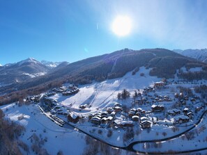 Ein verschneites Bergdorf mit Chalets, eine Skipiste und ein klarer, blauer Himmel.