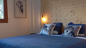 Een slaapkamer met een houten hoofdbord, een groot bed met blauw beddengoed en twee kussens met dierenprint.