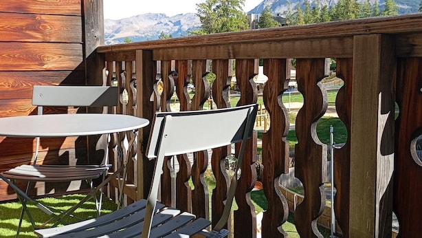Een houten terras met een tafel en stoelen, uitkijkend op een bergachtig landschap.