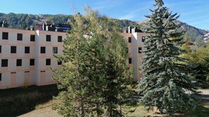A modern building with a grid-like facade, surrounded by trees and a mountainous backdrop.