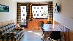 A room with a checkered sofa, a dining table with a patterned tablecloth, and a window with checkered curtains.