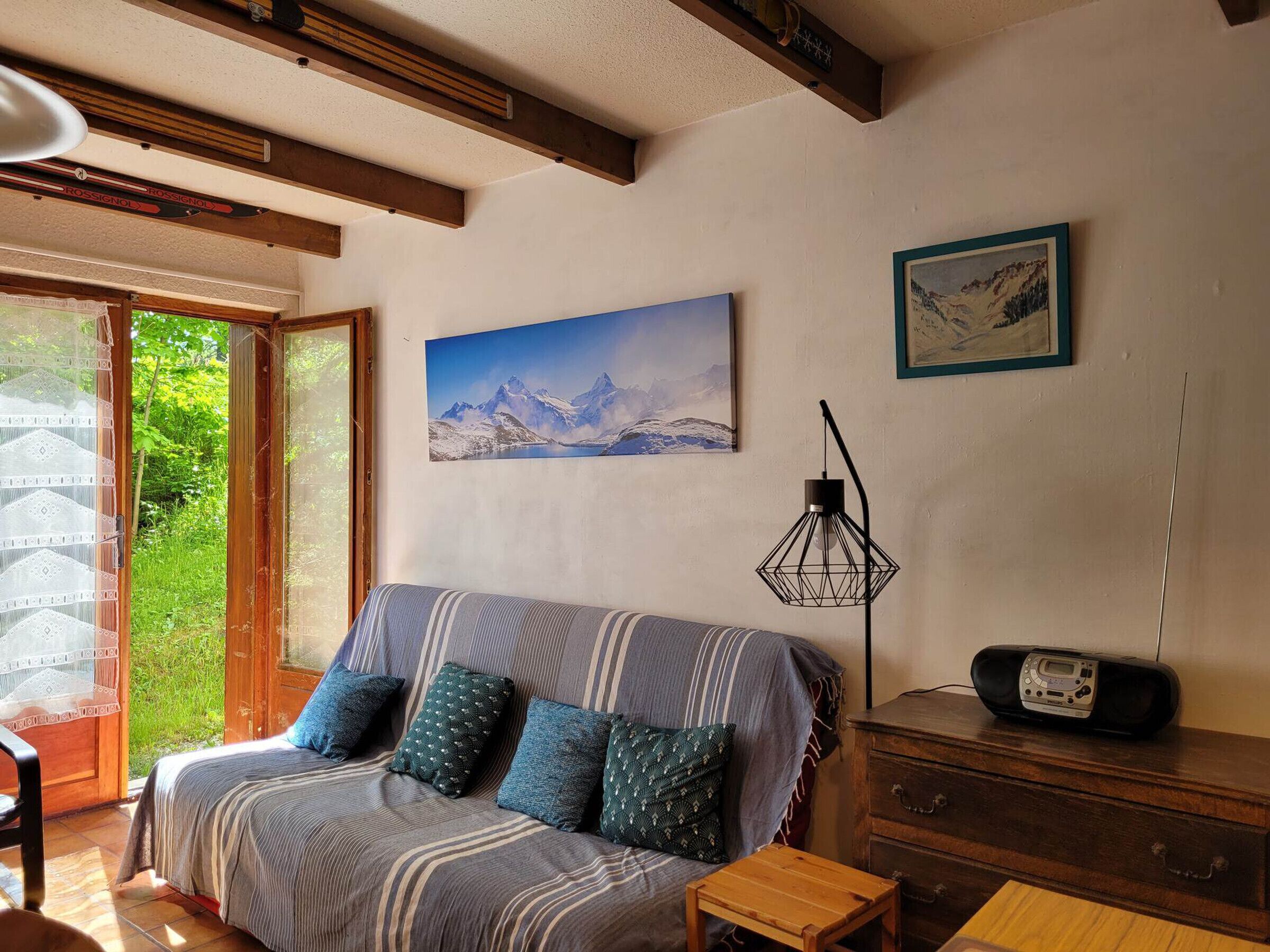 Ein gemütliches Zimmer mit einem Bett, einer Holzkommode, einem Radio und einem Bergpanorama.