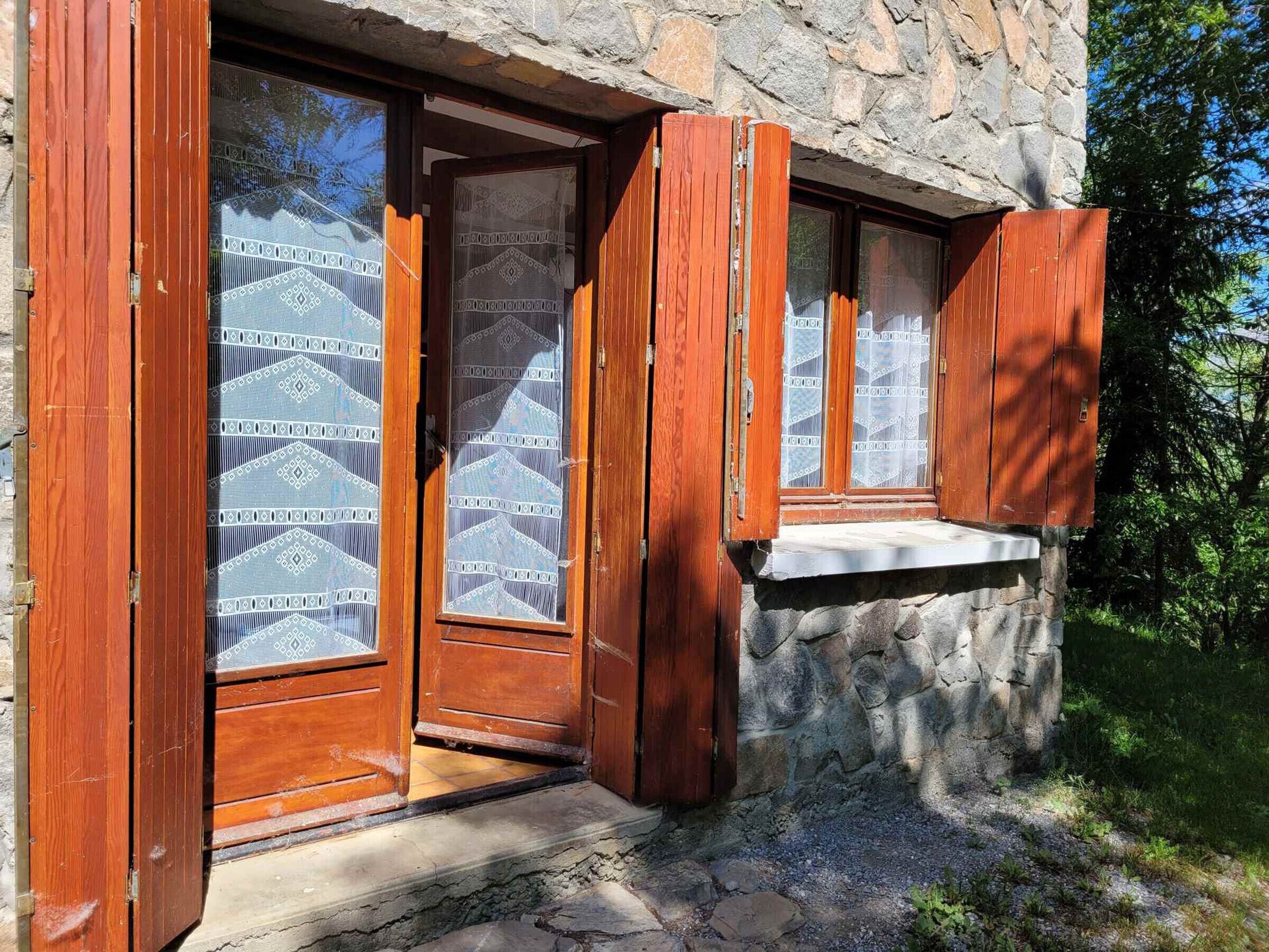 A stone building with wooden doors and windows, a stone wall, and a small ledge.