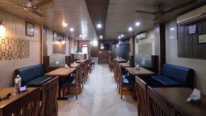 A restaurant with booths and tables, ceiling fans, and wall decorations. - Ambika Hotels (Faridabad)