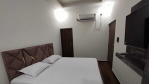 A bedroom with a bed, a TV, an air conditioning unit, and a door. - Ambika Hotels (Faridabad)