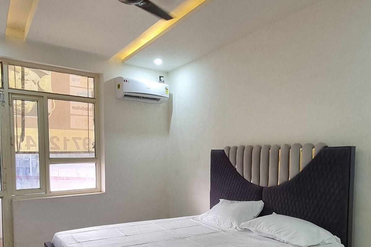 A bedroom with a bed, ceiling fan, air conditioning unit, and a window.