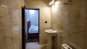 A modern bathroom with a marble floor, a pedestal sink, and a toilet. - Ambika Hotels (Faridabad)