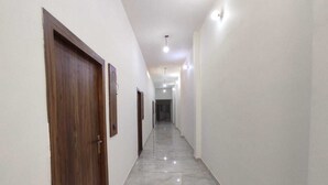 A corridor with marble flooring, white walls, and wooden doors. - Ambika Hotels (Faridabad)