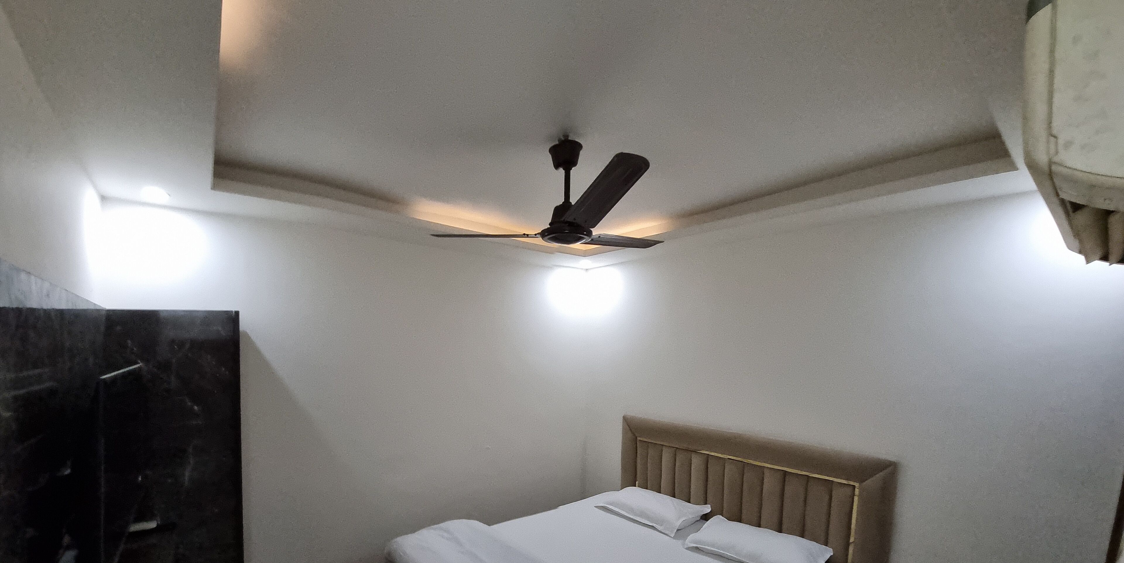 A hotel room with a bed, a ceiling fan, and a light fixture.