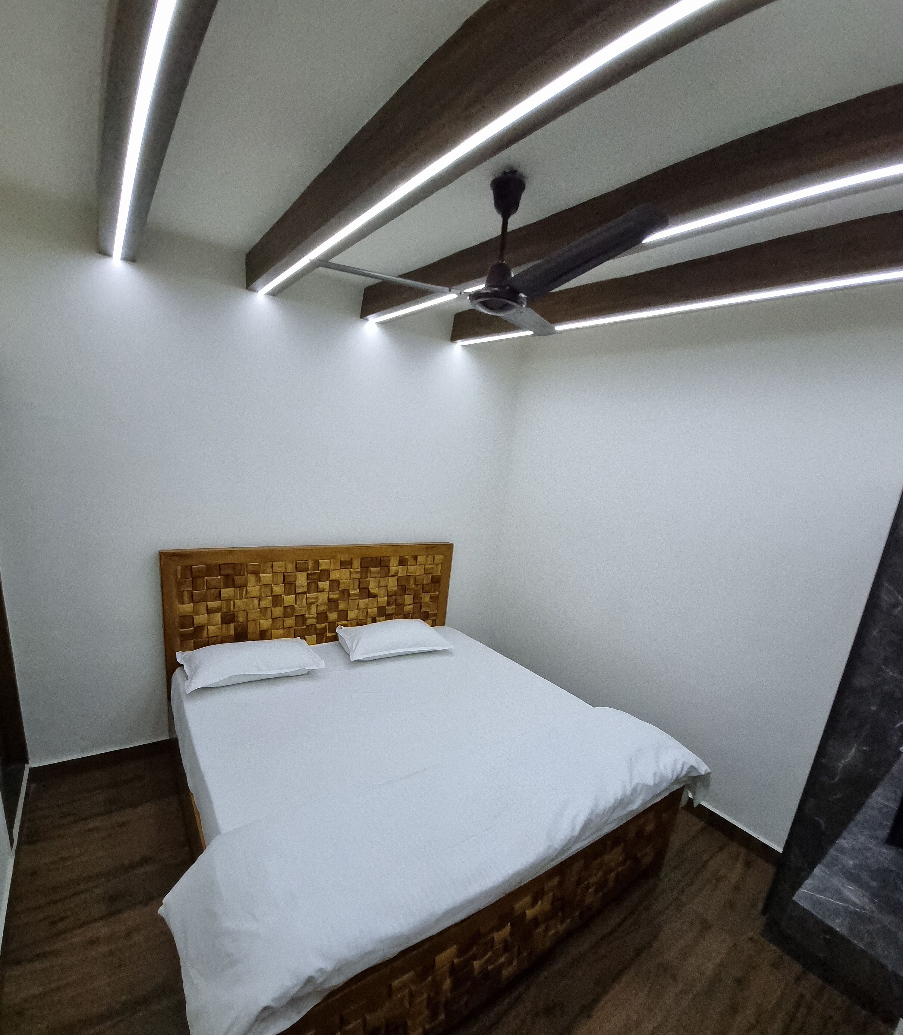 Ein Schlafzimmer mit Holz-Kopfteil, einem Bett mit weißer Bettwäsche, einem Deckenventilator und modernen Lampen.