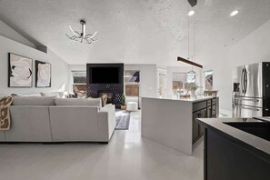A modern kitchen with a large island, a dining area with a sofa, and a living room with a fireplace.