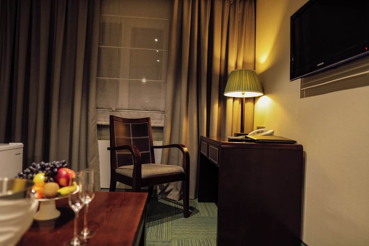 A hotel room with a wooden desk, a chair, a lamp, a TV, and a fruit bowl.