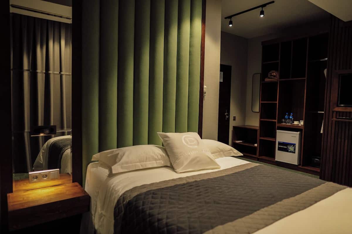 A hotel room with a bed, a nightstand, a mirror, a green curtain, and a wardrobe.
