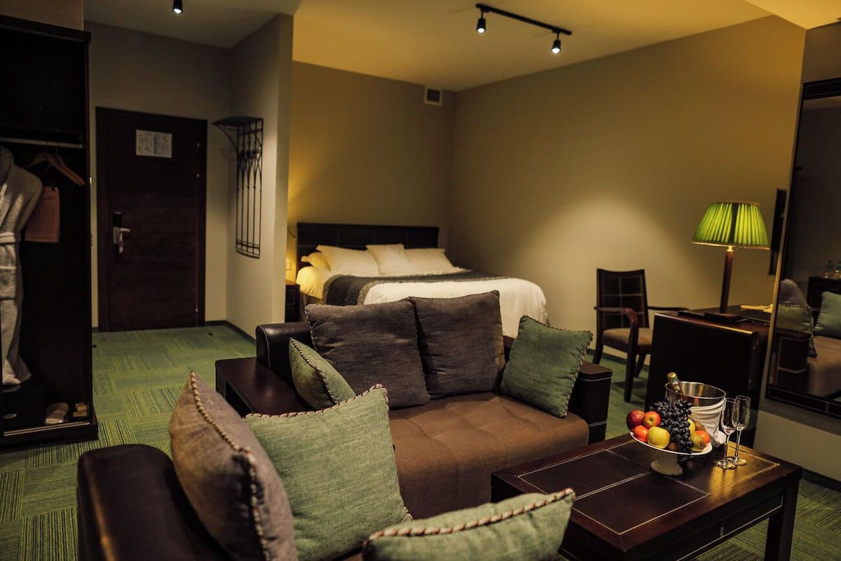 A hotel room with a bed, a sofa, a coffee table with fruit, and a mirror.