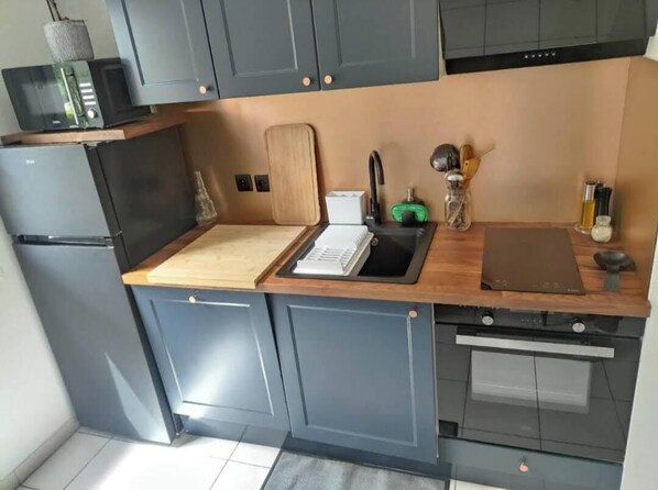 A compact kitchen with grey cabinets, a wooden countertop, a microwave, a toaster, and a sink.