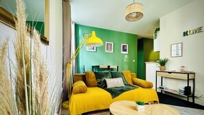 Ein modernes Schlafzimmer mit grüner Wand, einem gelben Bett, einer Nachttischlampe und einem kleinen runden Tisch.