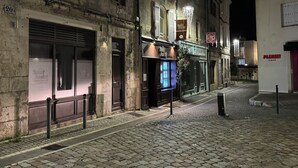 Una calle adoquinada de noche, con una hilera de edificios, incluyendo un escaparate visible con letreros iluminados.