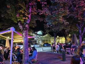 Un espace extérieur aménagé avec des tables et des chaises, entouré d’arbres et avec, en arrière-plan, un bâtiment doté de grandes fenêtres.
