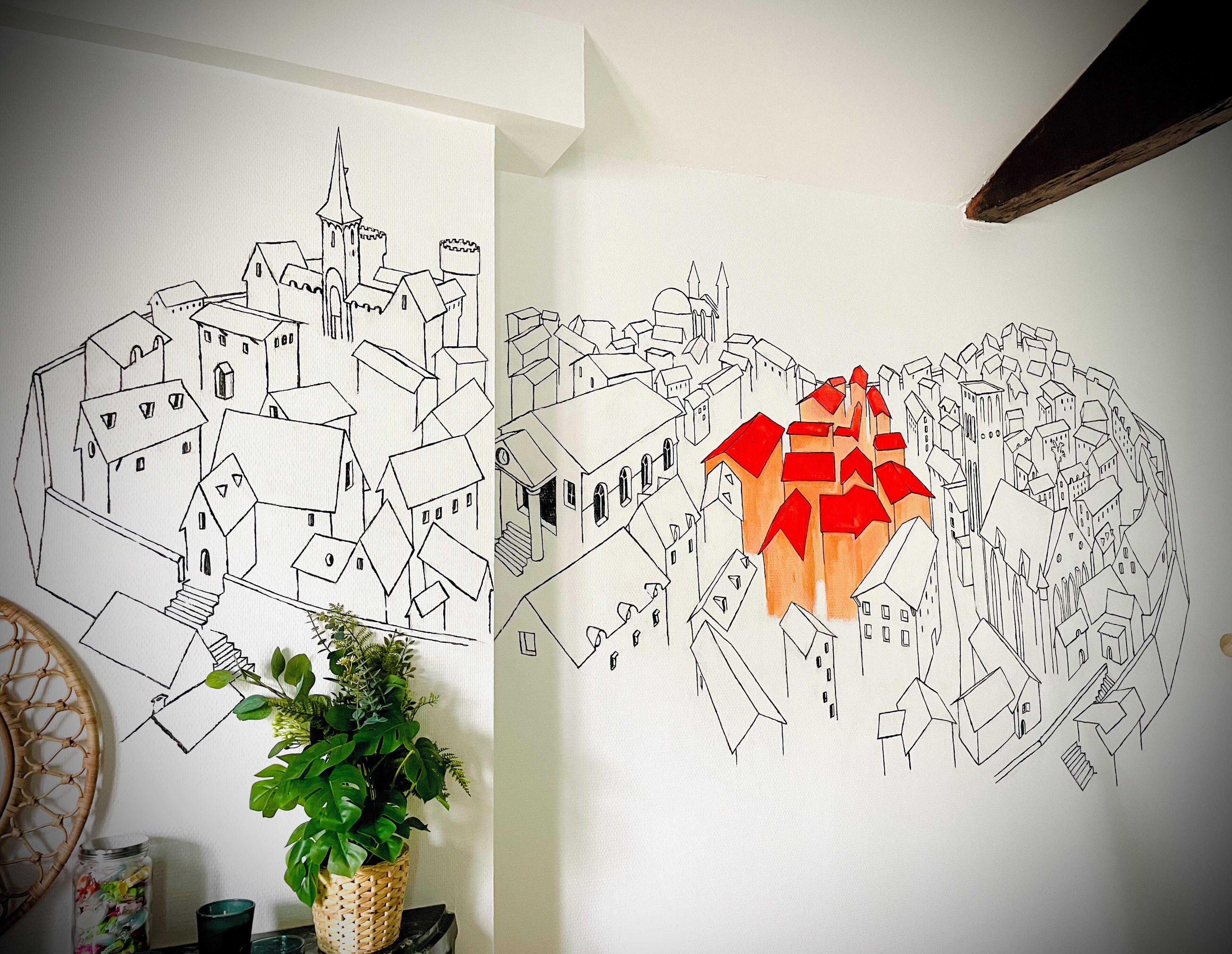 A wall with two line drawings of a town, one in black and one in red, with a potted plant in the foreground.